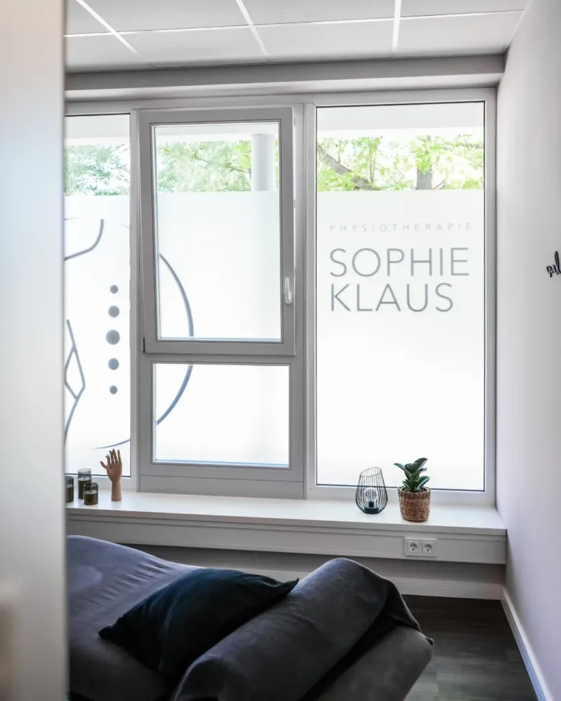 Behandlungsraum der Physiotherapie Sophie Klaus mit Fensterbeschriftung und Liege im warmen Tageslicht.