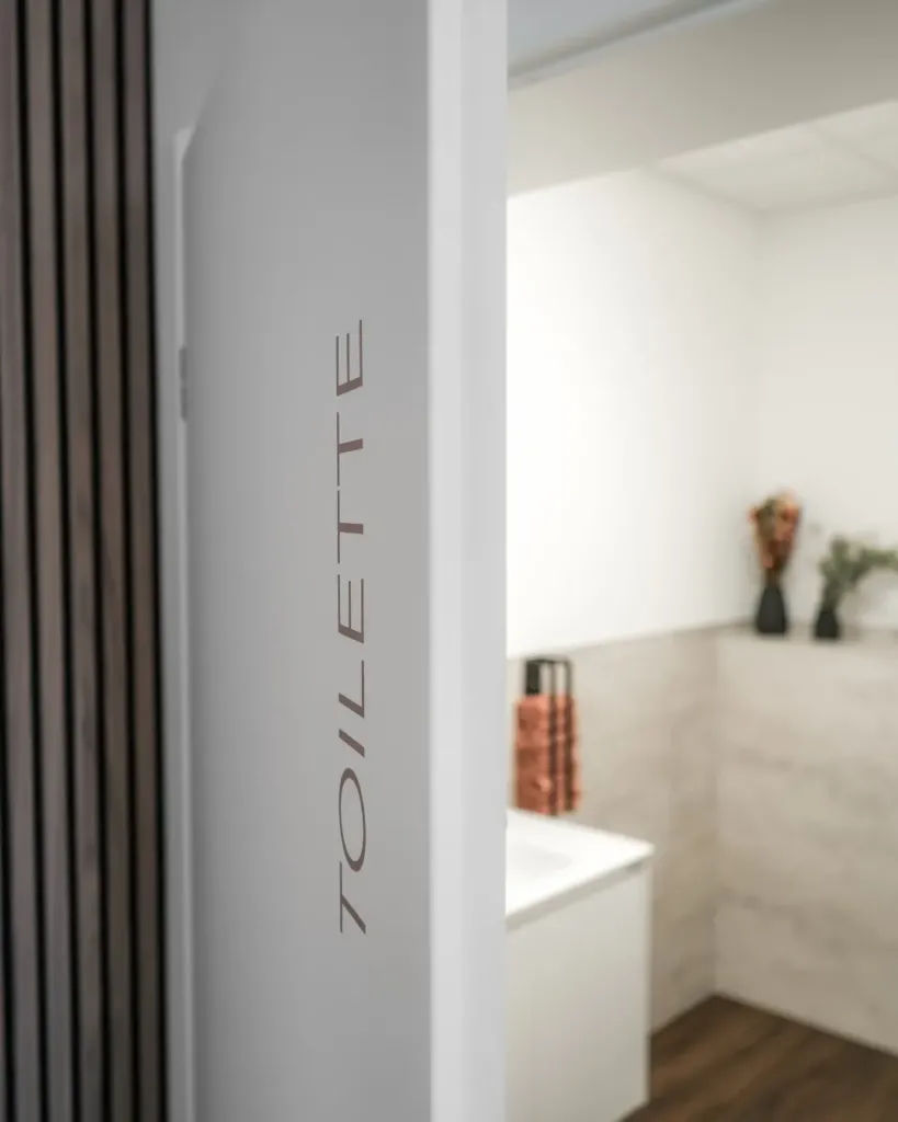 Türbeschriftung Toilette in der Physiotherapie Sophie Klaus, Blick auf modernes Badezimmer im Hintergrund