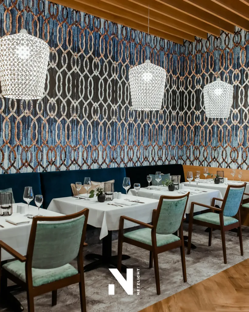 Gestalteter Gastraum eines Restaurants mit gemusterter Wandtapete, Hängeleuchten und eingedeckten Tischen für Weihnachtsfeiern.